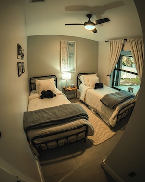 Un dormitorio con dos camas, un ventilador de techo, un mapa en la pared y una ventana con cortinas.
