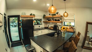 Une cuisine moderne dotée d’un îlot central, de luminaires suspendus et offrant une vue sur l’extérieur.