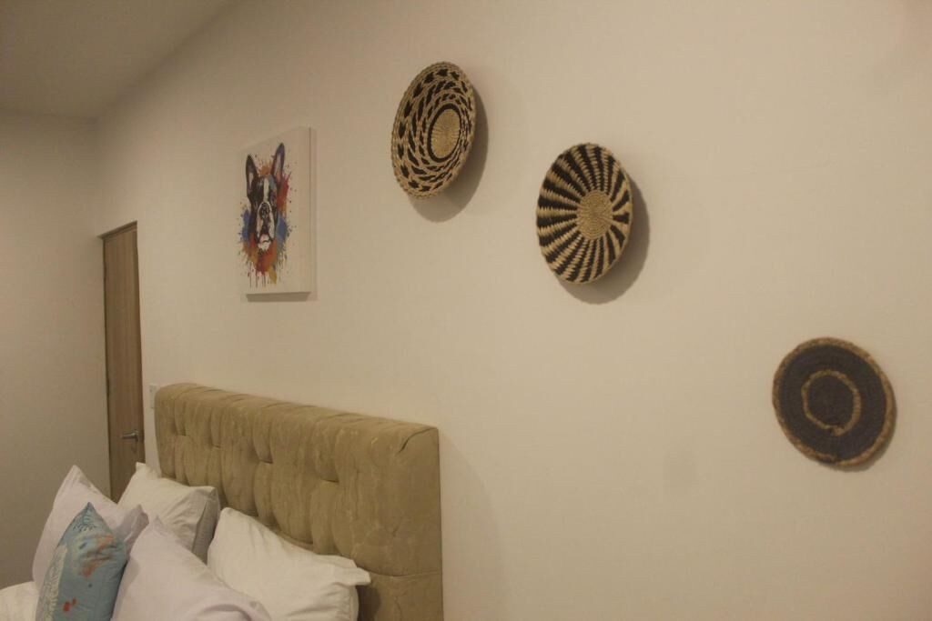 A bedroom with a tufted headboard, a bed with white and patterned pillows, and three woven wall hangings.