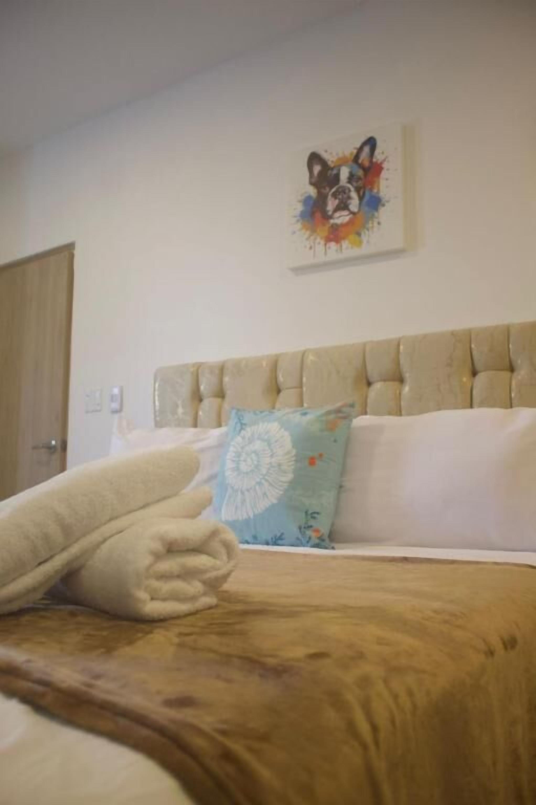 Una cama bien hecha con un cabecero color beige, una almohada de flores azules y una manta blanca.