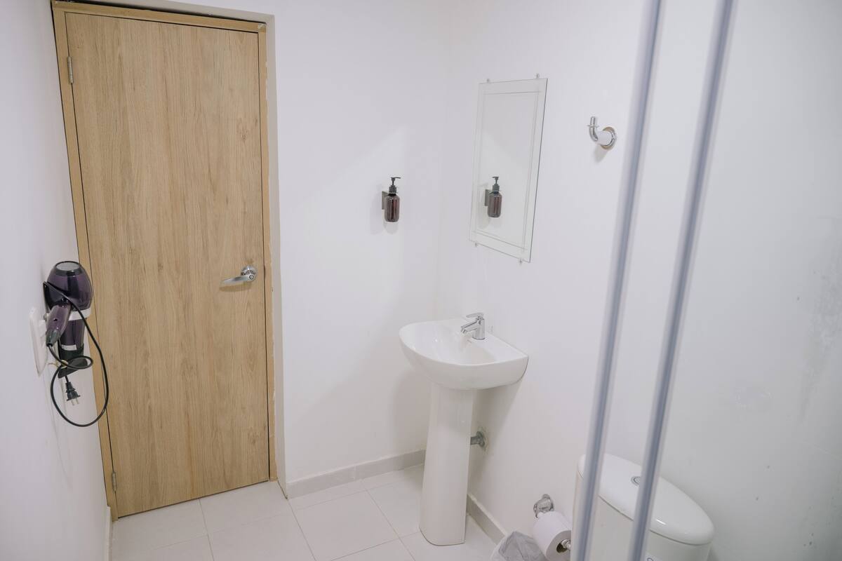 Egy fürdőszoba, amelyben fa ajtó, fehér mosdókagyló, tükör és WC található.