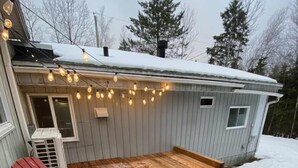 Una terraza de madera con un jacuzzi, sillas Adirondack rojas y luces colgantes.