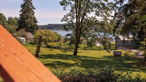 A wooden deck overlooking a grassy area with trees and a body of water in the background. - Bay View Casita in Olympia (Olympia)