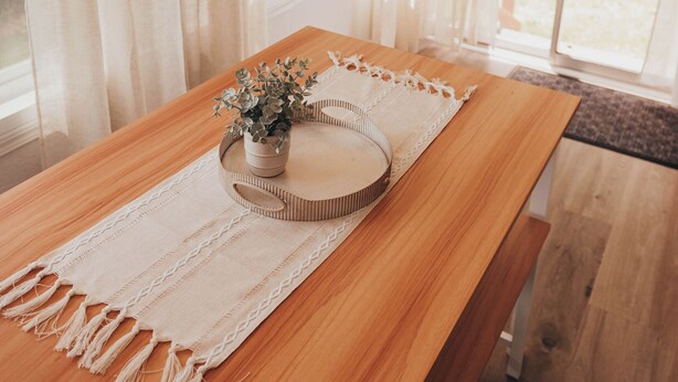 A wooden table with a beige macrame runner, a small potted plant, and a woven tray. - Bay View Casita in Olympia (Olympia)