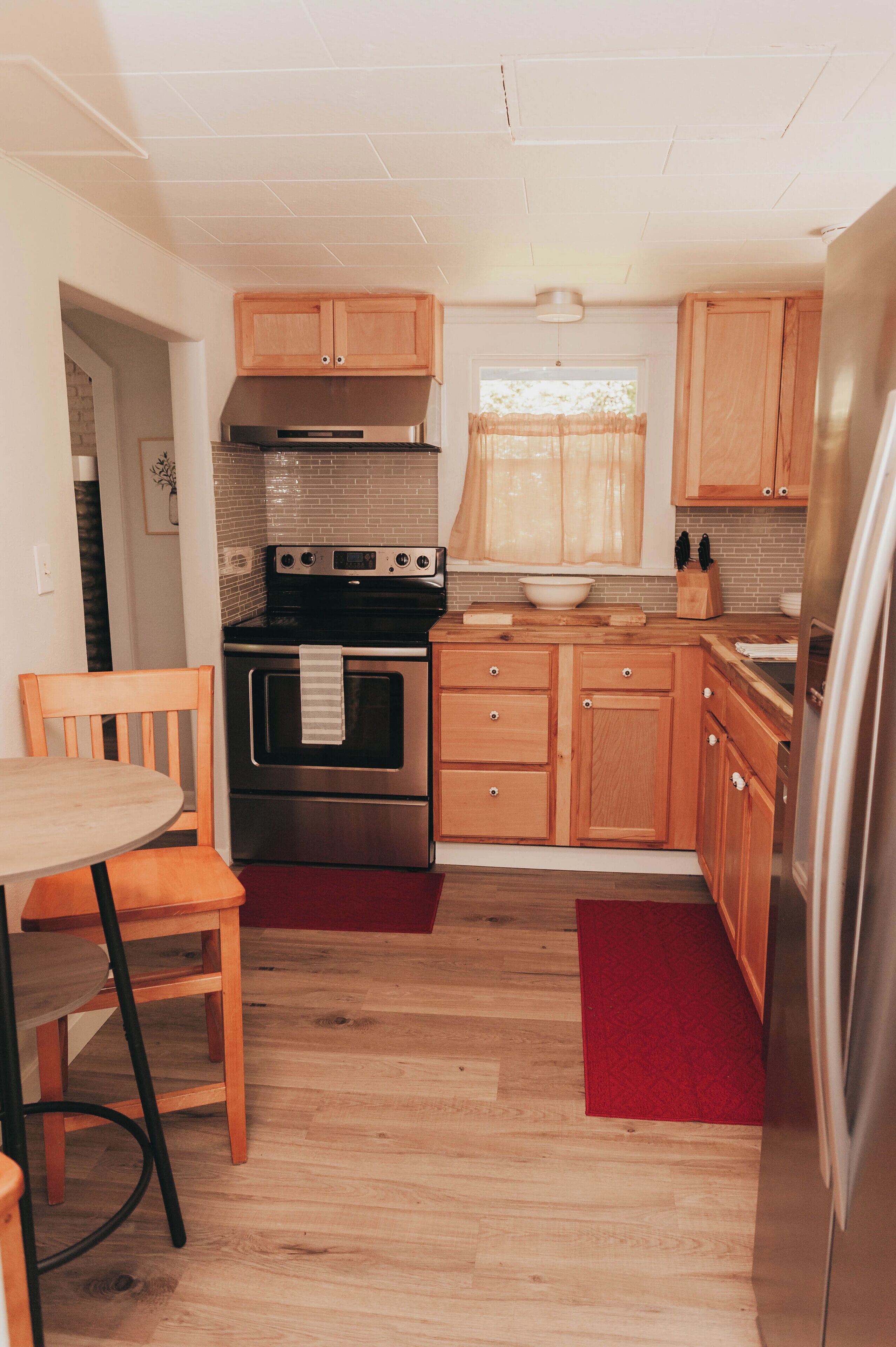 A compact kitchen with wooden cabinets, a stainless steel oven, and a dining area with a chair and table.