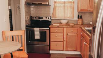 A compact kitchen with wooden cabinets, a stainless steel oven, and a dining area with a chair and table.