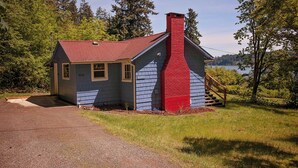 A small, single-story cabin with a red chimney, located near a body of water surrounded by trees. - Bay View Casita in Olympia (Olympia)