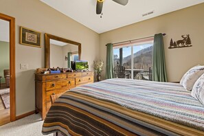 A bedroom with a large bed, wooden dresser, and a view of a mountainous landscape through a sliding glass door. - Fairway & Mountain Views, Relaxing 2BR Condo Retreat (Whittier)
