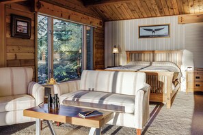 A cozy cabin interior with a large window, a bed, a sofa, and a table. - Hot Tub & Whale Watching! Scenic Sitka Escape (Sitka)