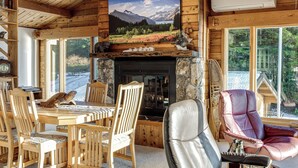 A cozy cabin interior with a stone fireplace, wooden furniture, and large windows offering scenic views. - Hot Tub & Whale Watching! Scenic Sitka Escape (Sitka)