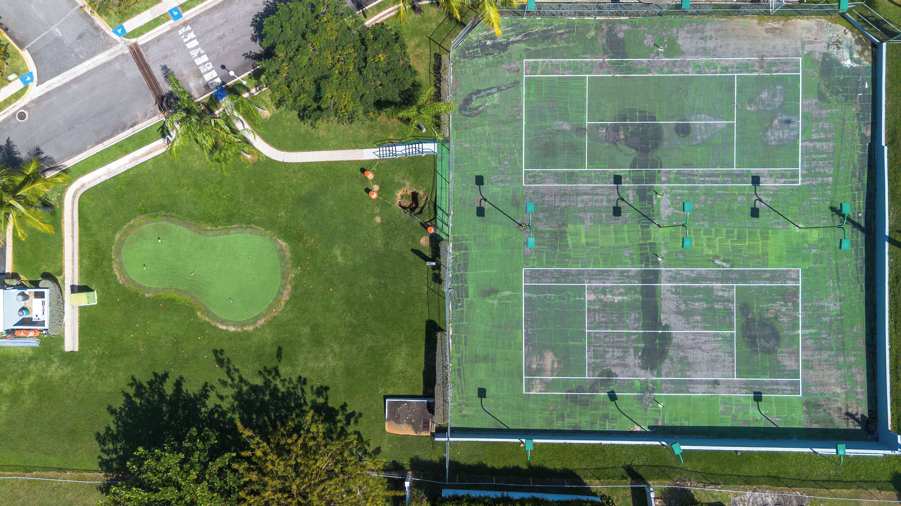 Vista aérea de un complejo deportivo con cancha de tenis, campo de golf y zonas verdes circundantes.