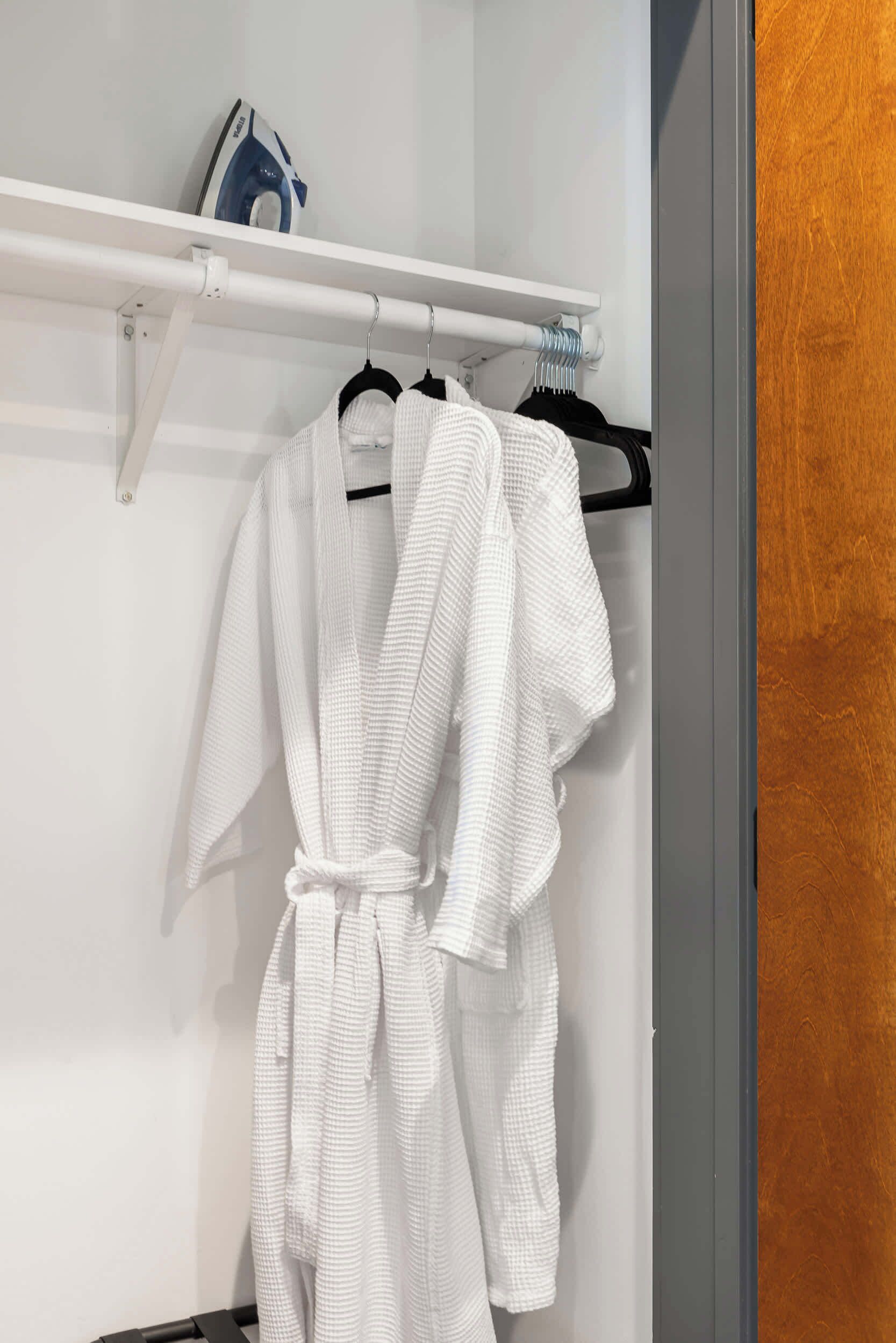 A white robe hanging on a rack in a bathroom with a wooden door and a white towel rack.