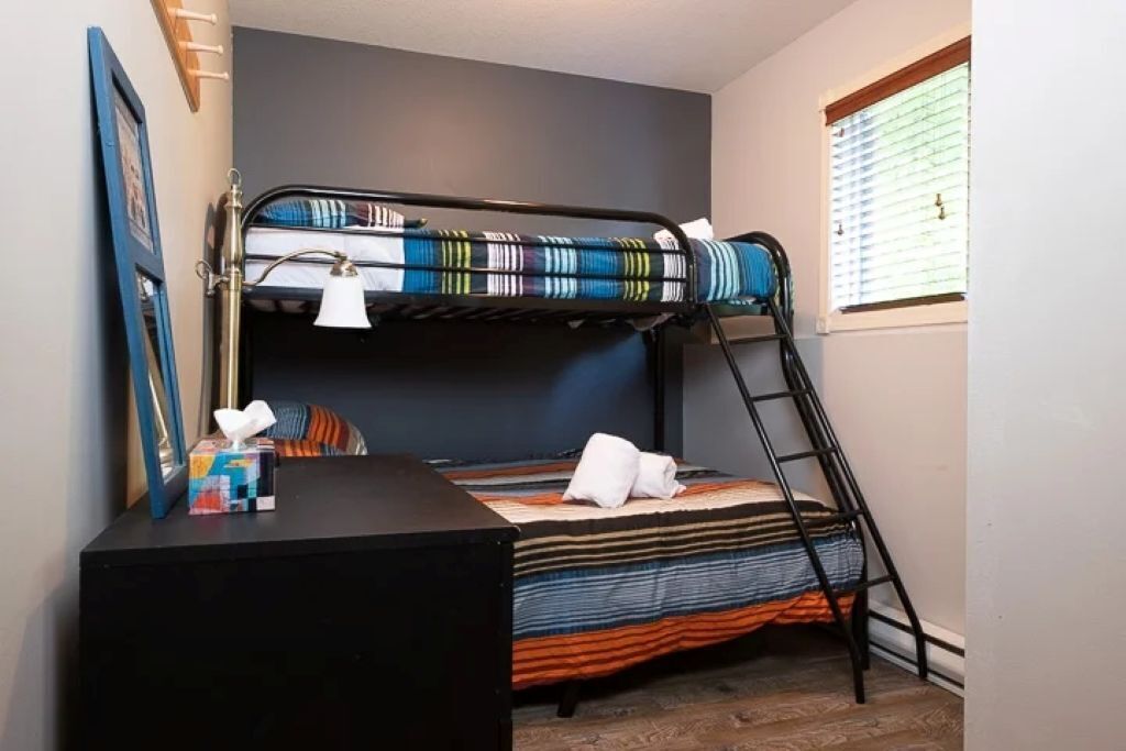A bunk bed with a ladder, a bedside table with a lamp, and a window with blinds.