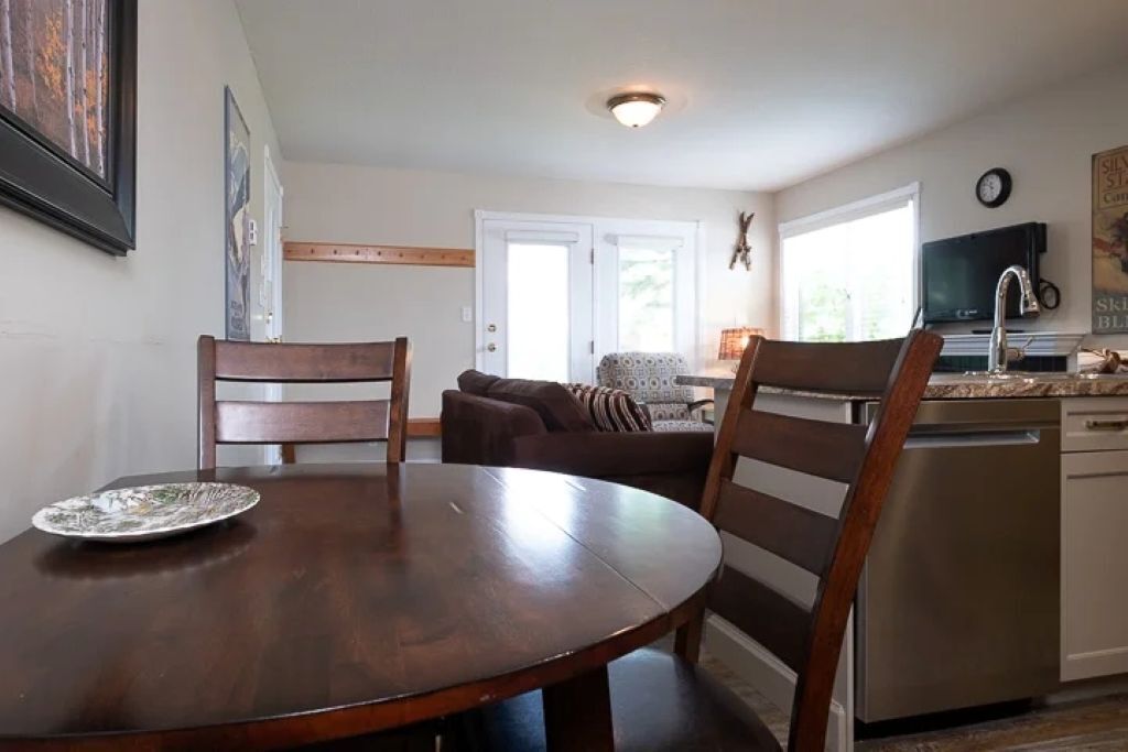 A dining area with a round wooden table and two chairs, a kitchen with a dishwasher, and a living area with a couch and a television.