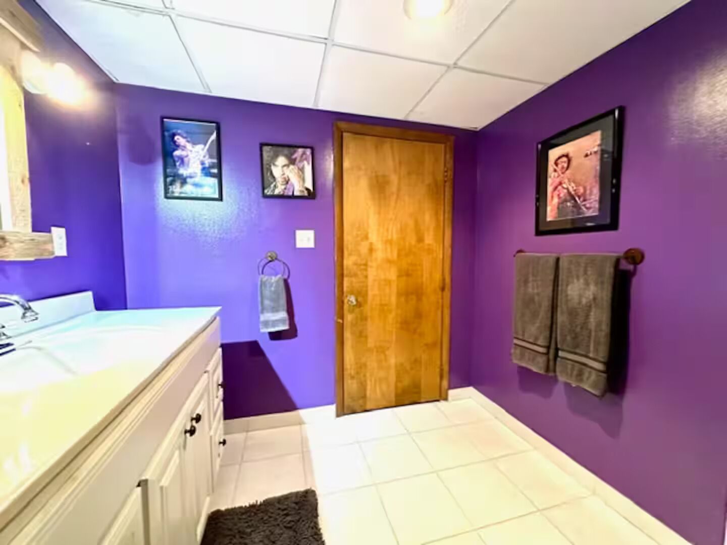 A bathroom with purple walls, a wooden door, a white sink, and two framed pictures on the wall.