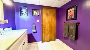 A bathroom with purple walls, a wooden door, a white sink, and two framed pictures on the wall.