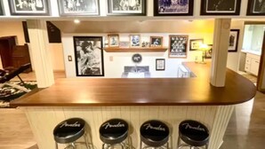 Un coin bar avec un comptoir en bois et trois tabourets. Au-dessus du comptoir, des photographies encadrées sont accrochées au mur.