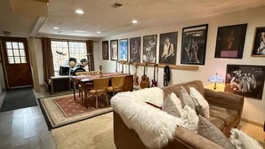 Un salon avec un canapé, une table à manger et des chaises. On peut voir des guitares accrochées au mur et des tableaux encadrés.