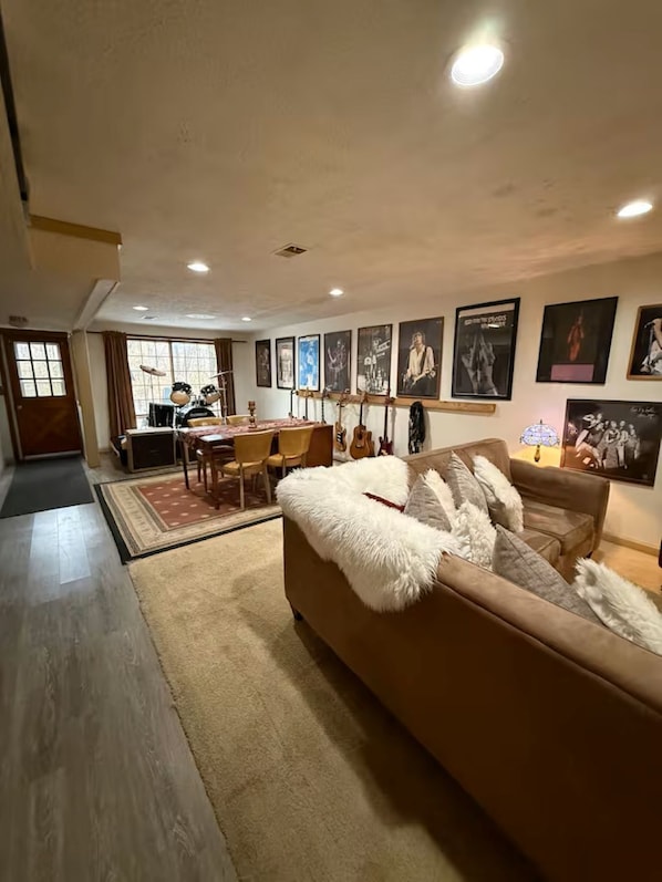 A living room with a sofa, a dining table, and chairs. There are guitars on the wall and framed pictures on the wall.