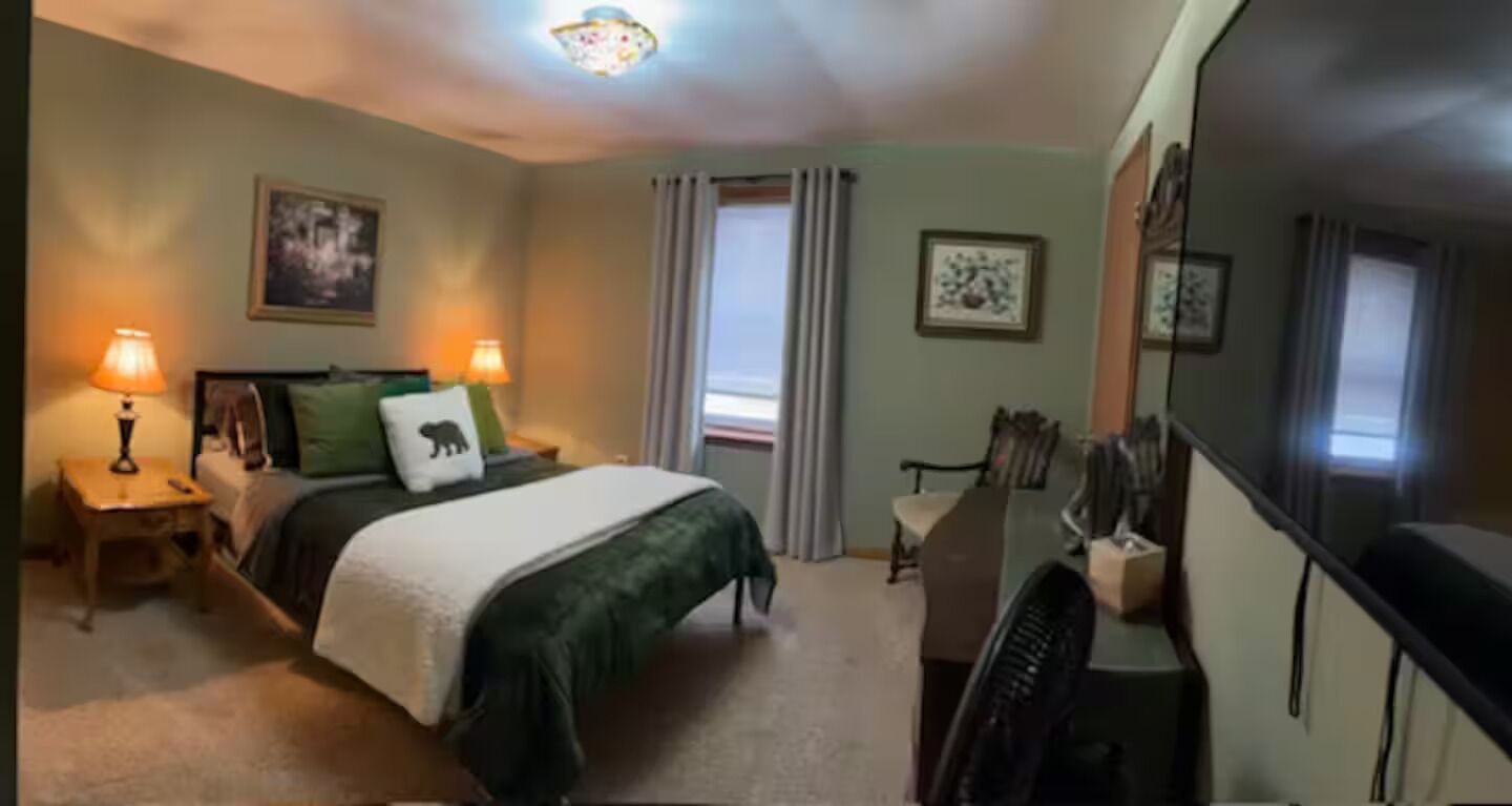 A hotel room with a bed, two bedside lamps, a desk with a chair, and a large mirror.
