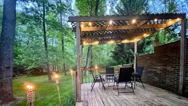 Une terrasse en bois agrémentée d’une pergola, de sièges d’extérieur et de guirlandes lumineuses.