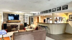 Un salon moderne avec une cheminée, un canapé et un téléviseur. Il y a également un coin cuisine avec un bar et des tableaux encadrés accrochés au mur.