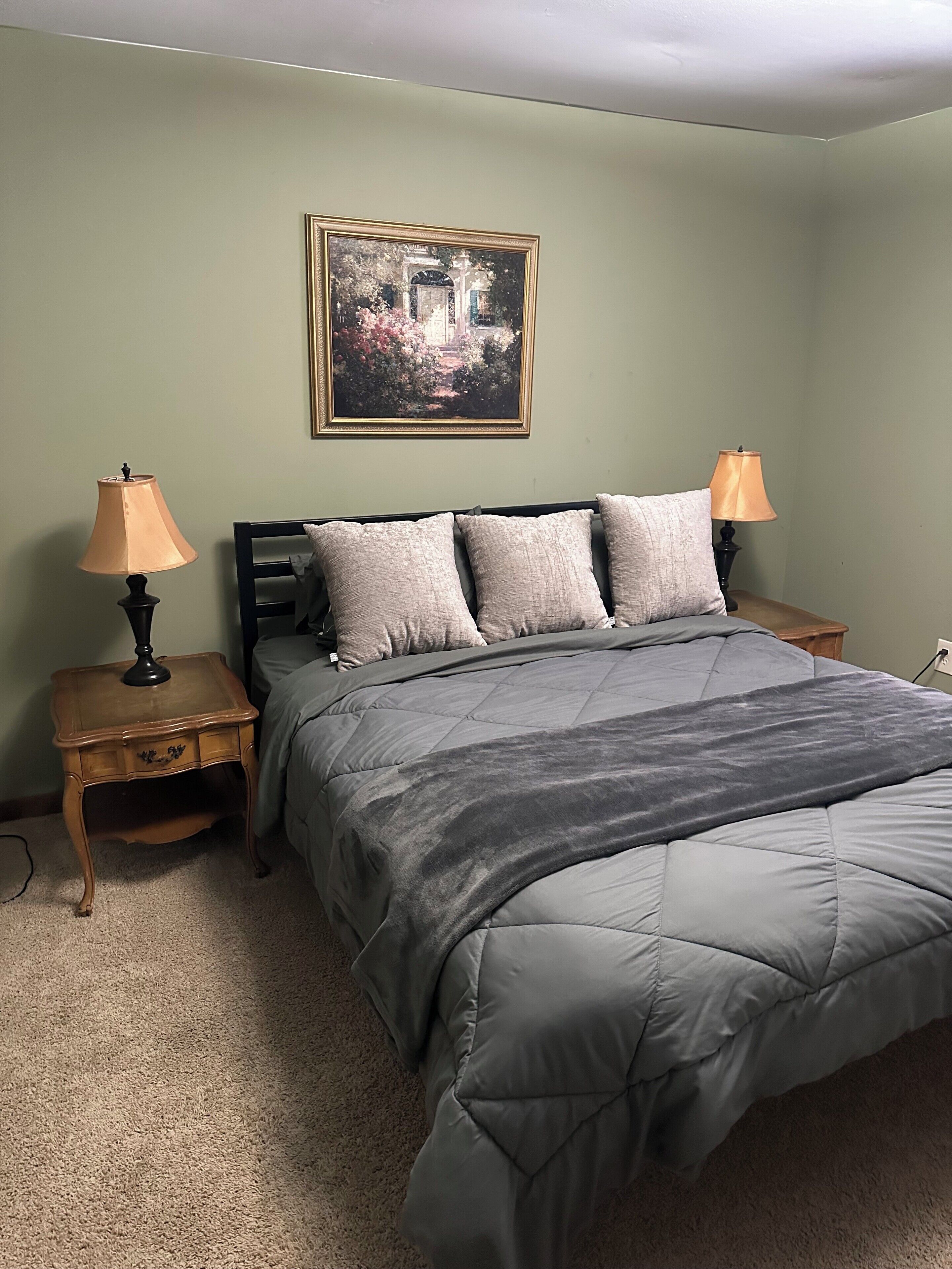 A bedroom with a bed, two nightstands, a lamp on each, and a framed picture on the wall.