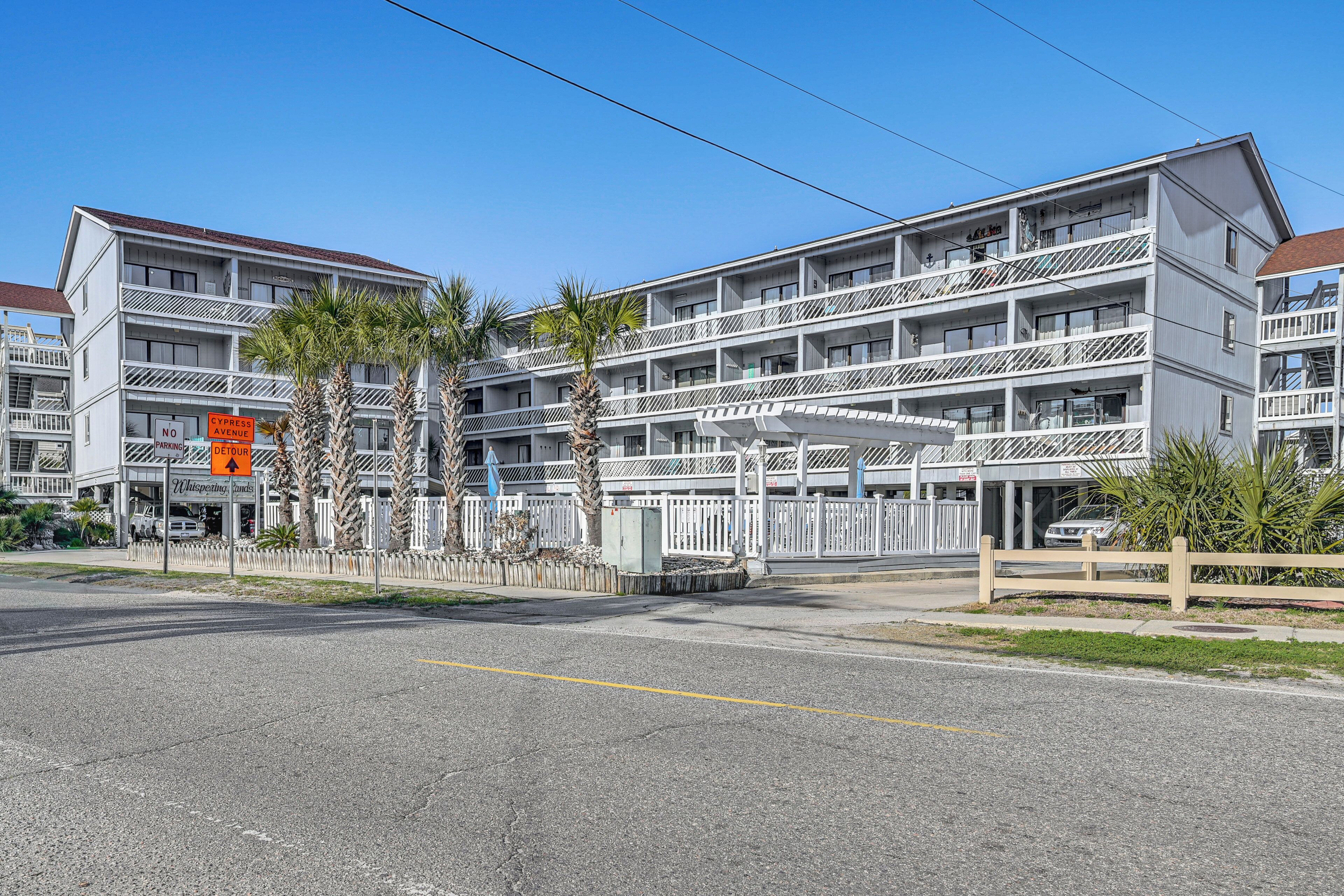 A multi-story motel with balconies, a parking area, and palm trees.