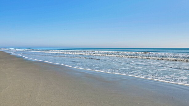 Een strand met een heldere lucht en een kalme zee.