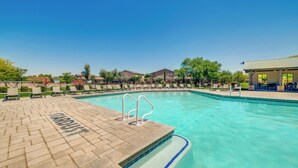 Ein Pool mit gefliestem Deck, Liegestühlen und einer überdachten Sitzgruppe.
