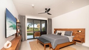 A modern bedroom with a large bed, a bench, a TV, and a ceiling fan. - Stunning Condo at The Pearl in Jaco Beach 4B (Jacó)