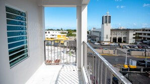 Un balcone con vista su un parcheggio e palazzi, tra cui una chiesa con una croce.