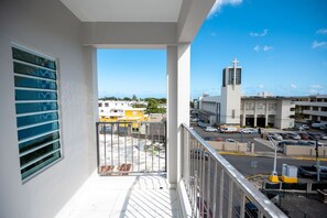 A balcony with a view of a parking lot and buildings, including a church with a cross. - Penthouse Apartment by the Beach (San Juan)