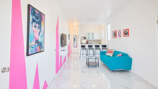 A modern living room with a teal sofa, a dining area with chairs, and a kitchen in the background. - Cozy Escape | Steps from Beach (San Juan)