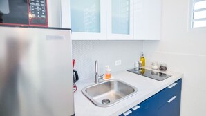 A modern kitchen with a stainless steel sink, a red faucet, and a white countertop. There are blue cabinets and a white backsplash. - Cozy Escape | Steps from Beach (San Juan)