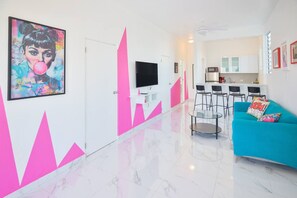 Een moderne woonkamer met een blauwgroene bank, een flatscreen televisie en een keuken in de achtergrond.