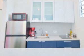 Een keuken met een koelkast, magnetron, koffiezetapparaat, spoelbak en kastjes.