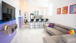 A modern living room with a sofa, a TV, and a kitchen in the background. - Modern Retreat By The Beach (San Juan)