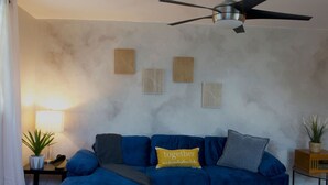 Ein Wohnzimmer mit blauem Sofa, Deckenventilator und Wandbildern.