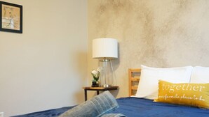 Ein ordentlich bezogenes Bett mit gerolltem Handtuch, einer Nachttischlampe und einem Kissen mit Schrift.