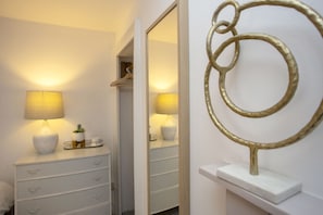 Ein Schlafzimmer mit Nachttisch, Lampe, Spiegel und einer dekorativen Metallskulptur an der Wand.