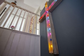 A wooden cross with colorful lights, a white railing, and a window with floral curtains.