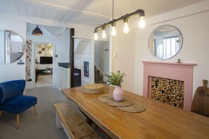 A dining area with a wooden table, benches, a blue chair, a pink vase with plants, and a fireplace with a mirror above it. - The Old Crescent Bakery - Beautiful Bath Townhouse (Bath)