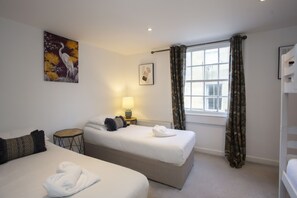 A hotel room with two beds, a window with curtains, a lamp, and artwork on the wall.