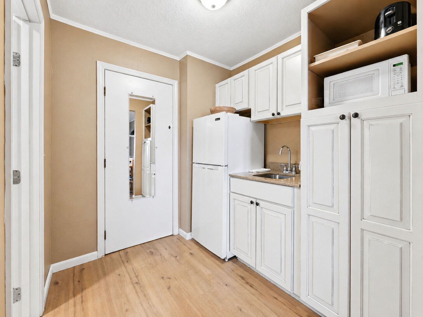A compact kitchen with white cabinetry, a built-in microwave, and a small countertop sink.