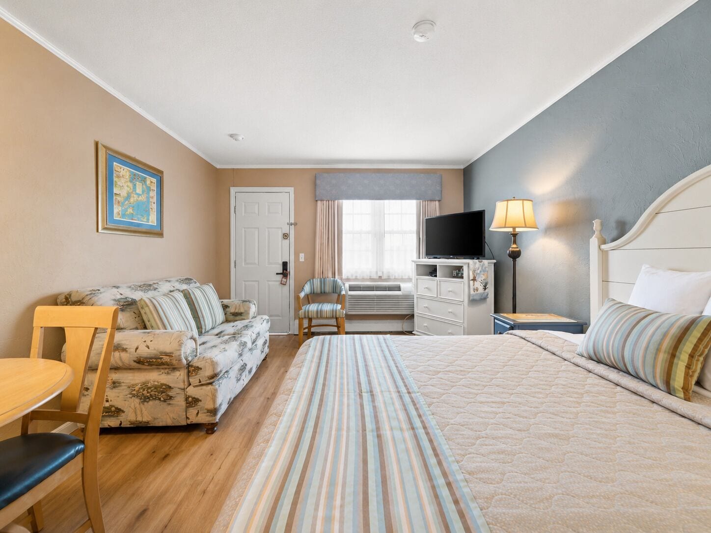 A hotel room with a bed, a sofa, a chair, a desk, a television, and a lamp.