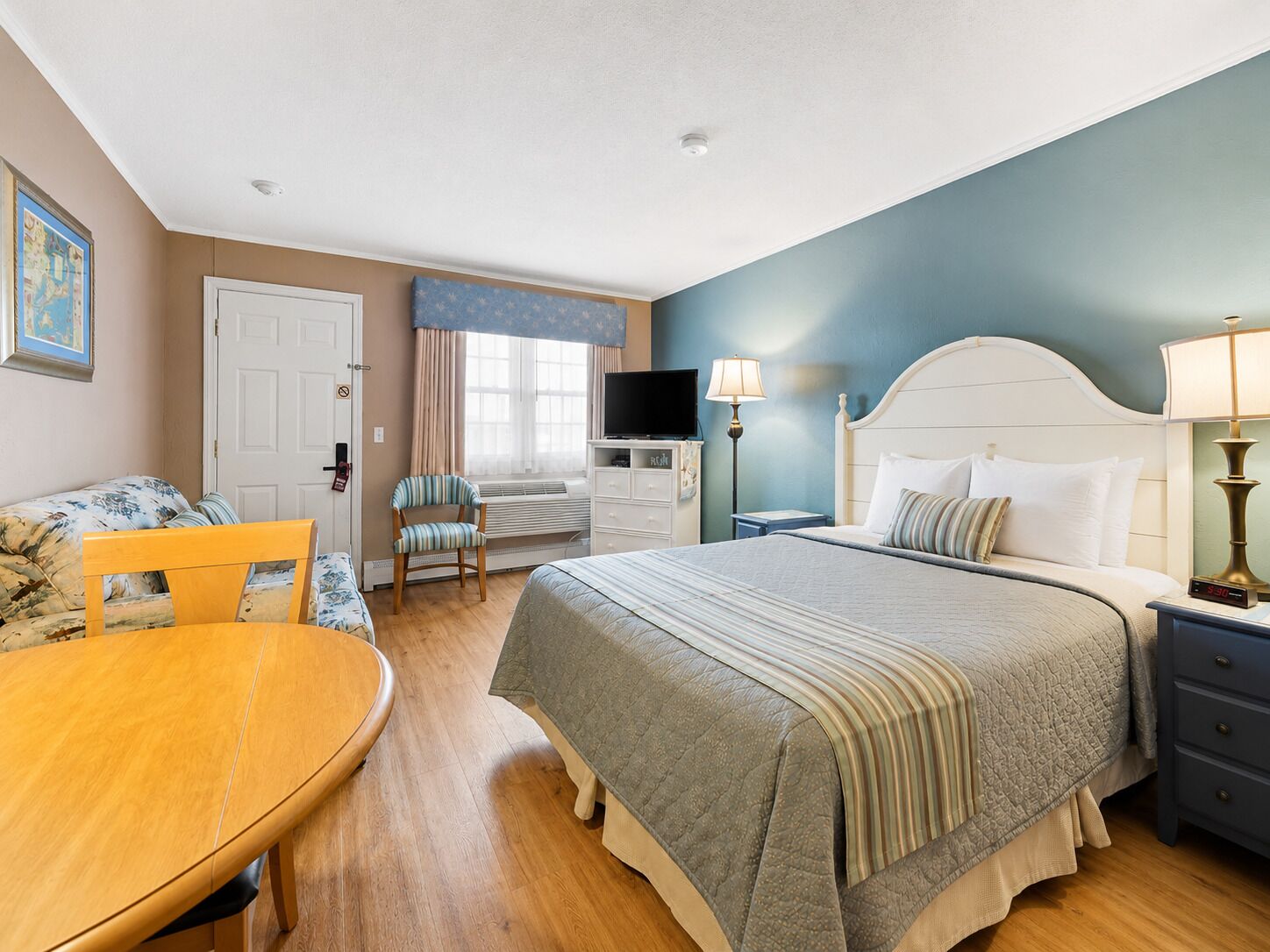 A hotel room with a bed, a desk, a chair, a television, and a lamp.