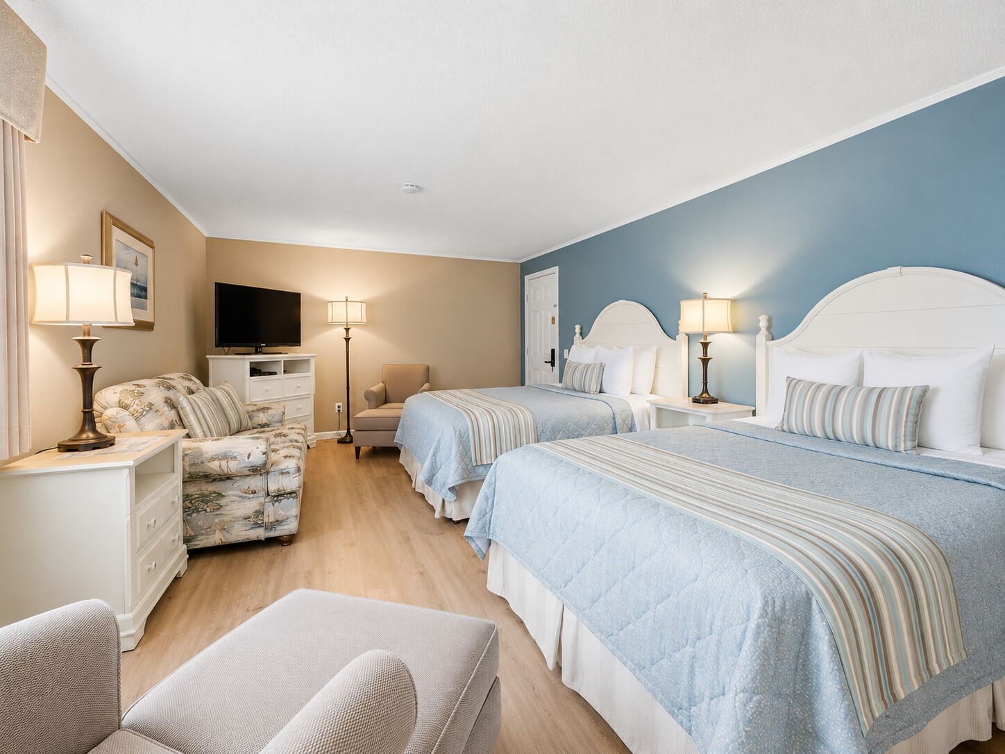 A hotel room with two beds, a TV, a chair, and a dresser.