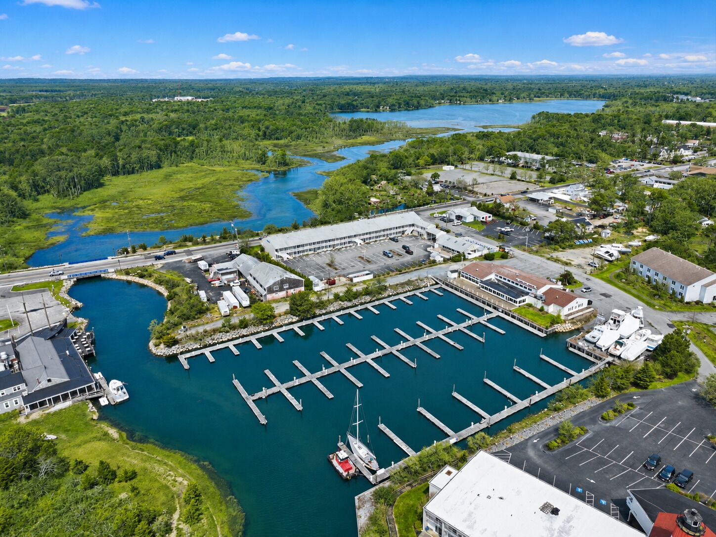 An aerial view of a marina with docks, a large parking area, and surrounding greenery.