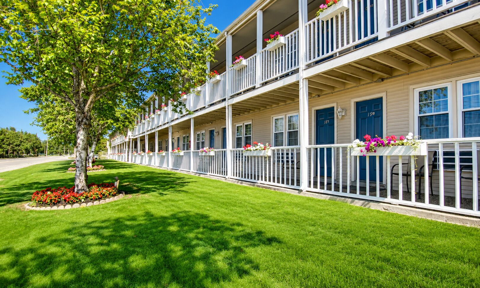 Un hilero de casas adosadas de dos pisos con balcones, un césped bien cuidado y jardineras con flores.